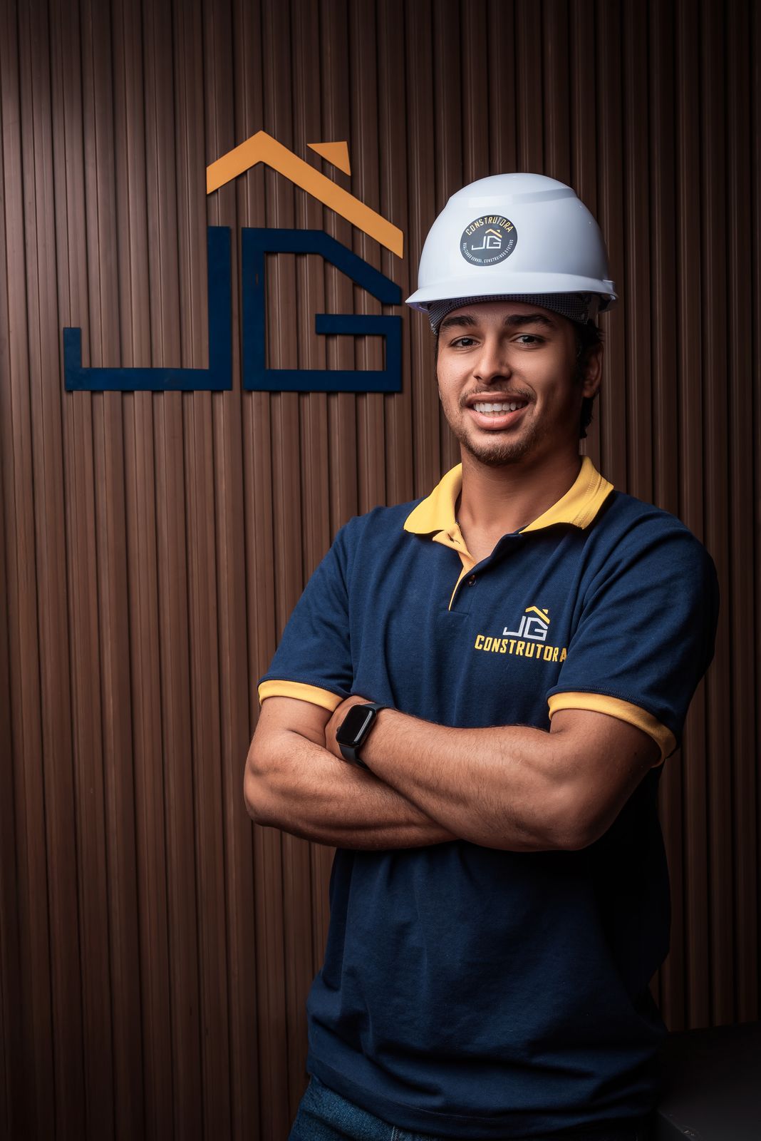 Juan, da JG Construtora, de uniforme e capacete em frente à logo da empresa